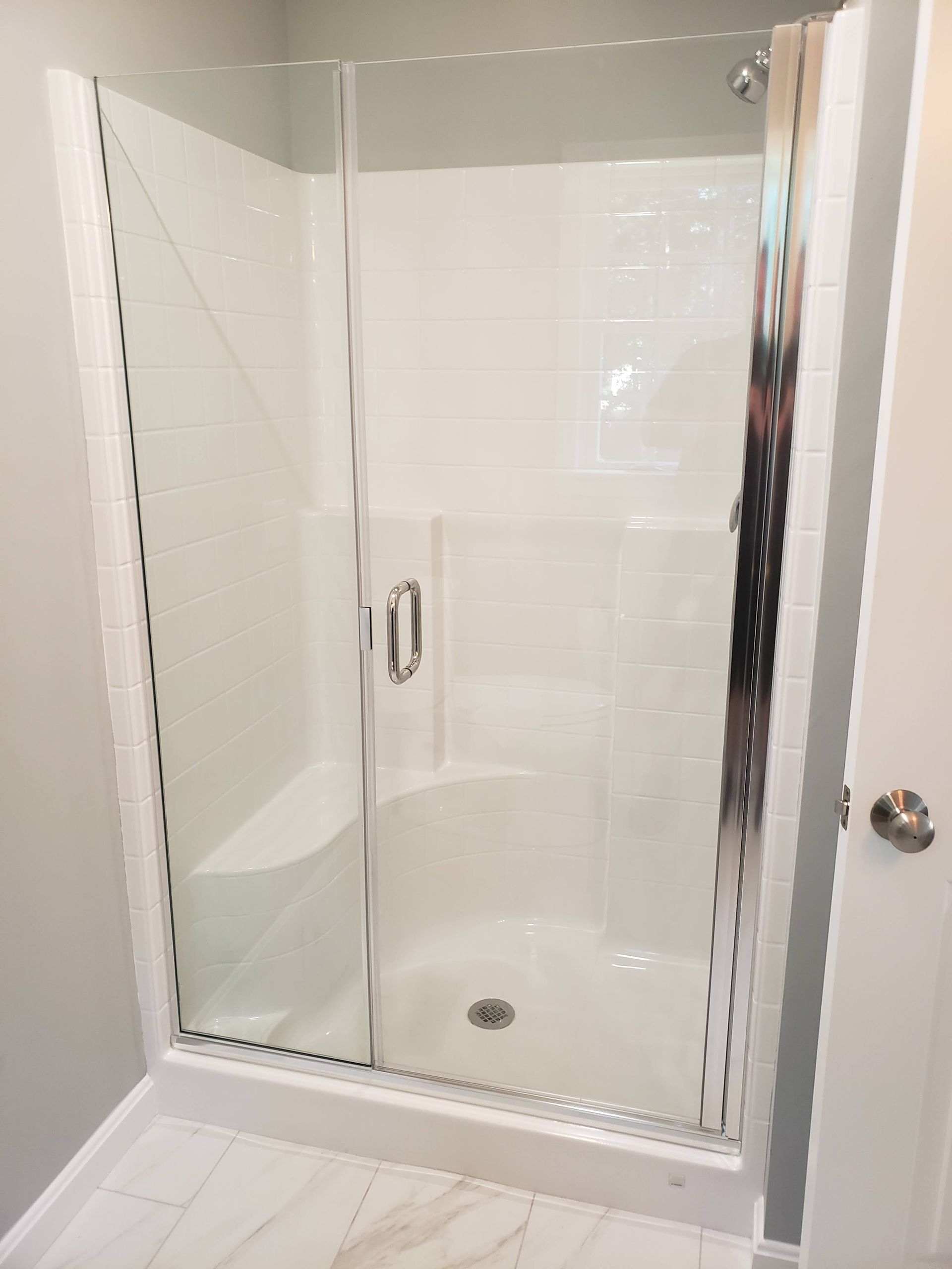 Glass shower enclosure with white tiled walls and a small built-in bench.