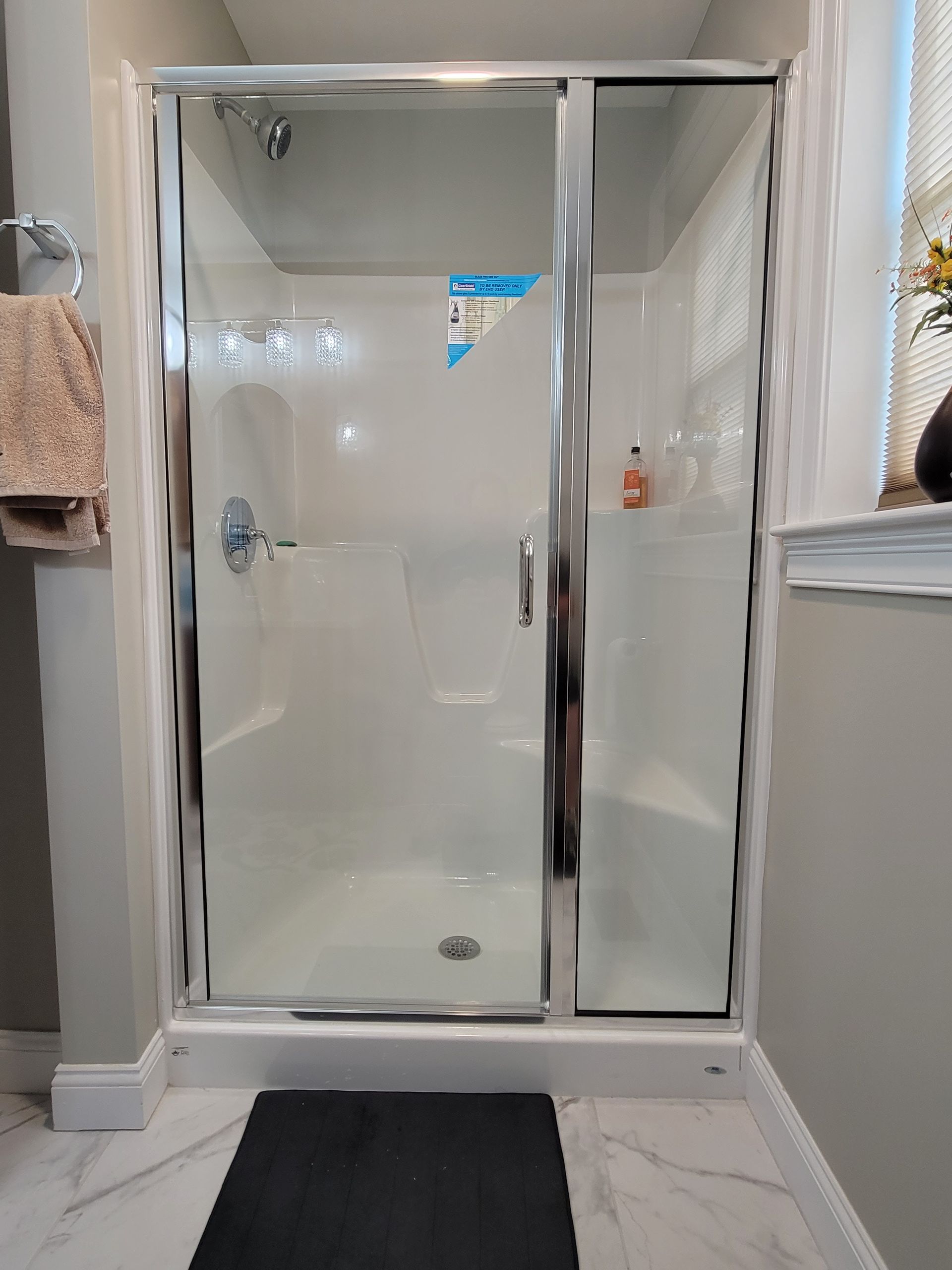 Shower stall with sliding glass doors, white walls, and a black mat in front.