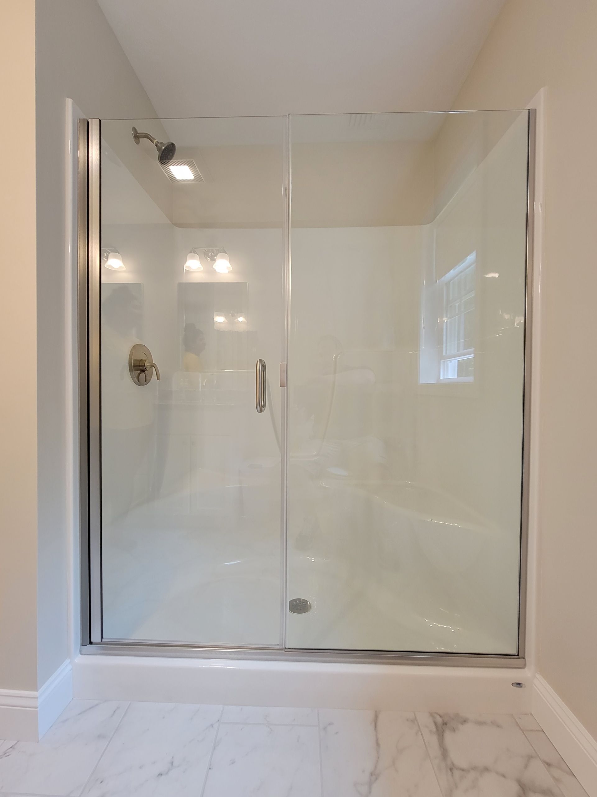 Glass shower enclosure with sliding door, silver trim, and marble floor.