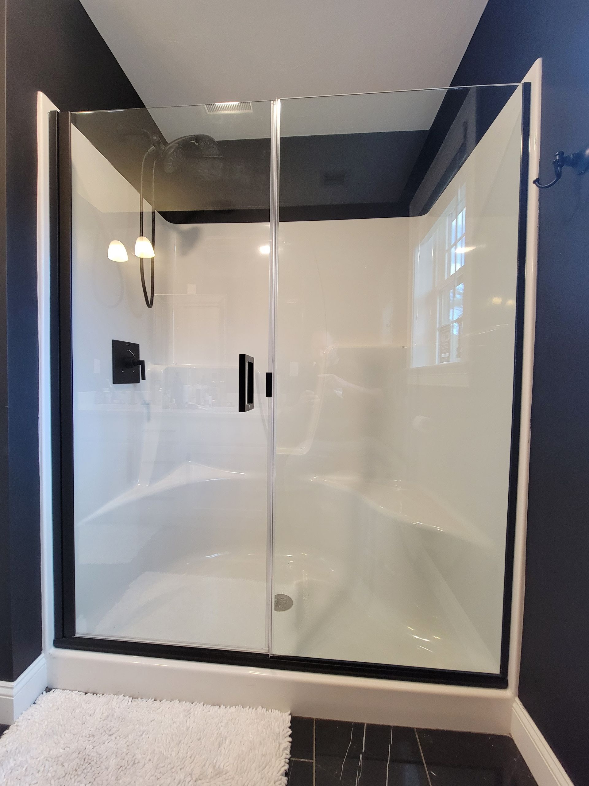 White shower stall with black trim, glass doors, and dark wall.