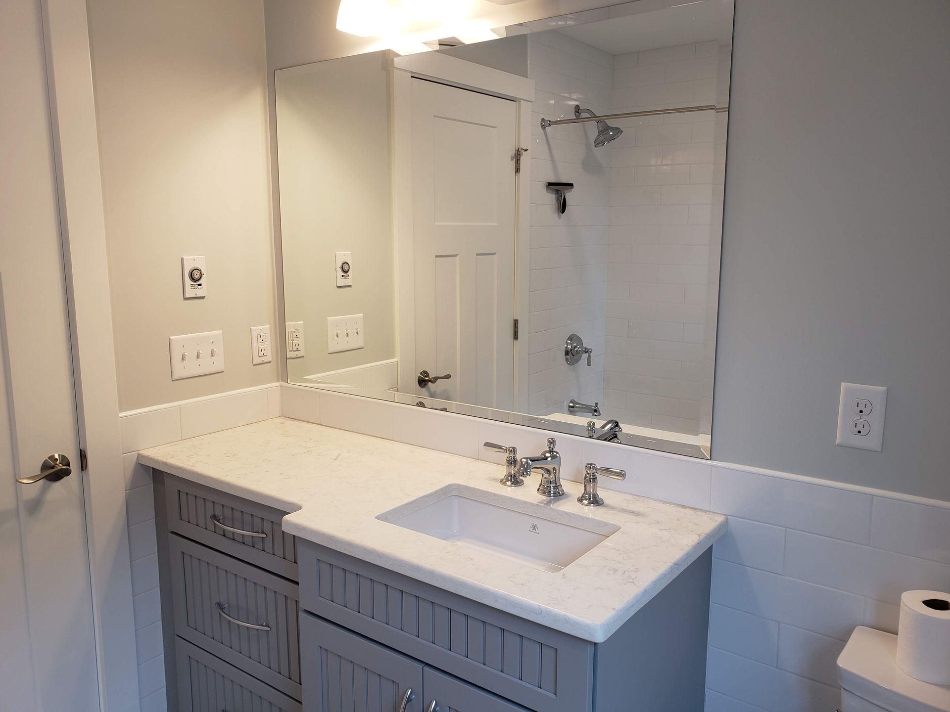 Bathroom with gray vanity, white countertop, large mirror, and recessed lighting.