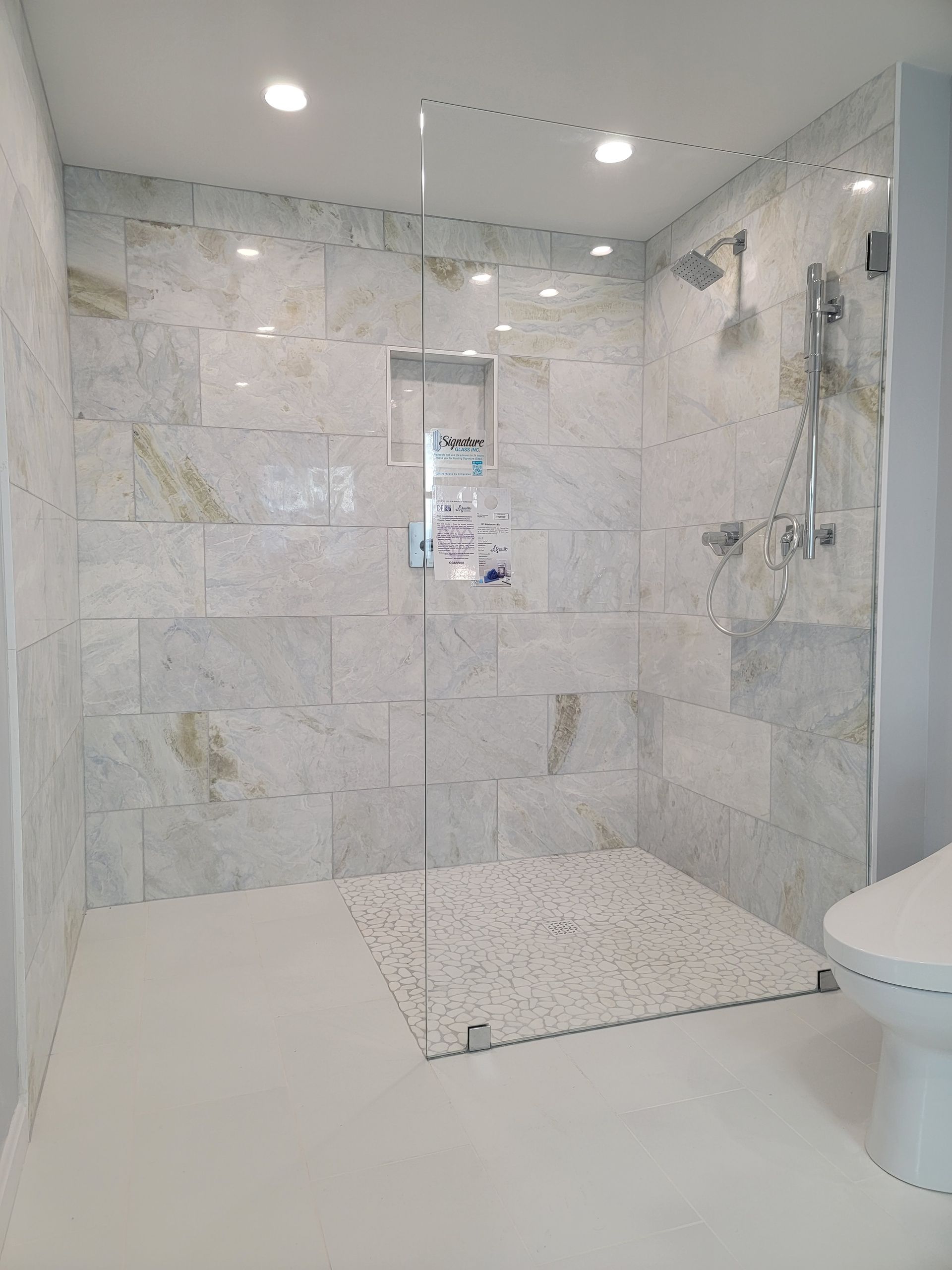 Accessible shower stall with light marble tile and a low entry.