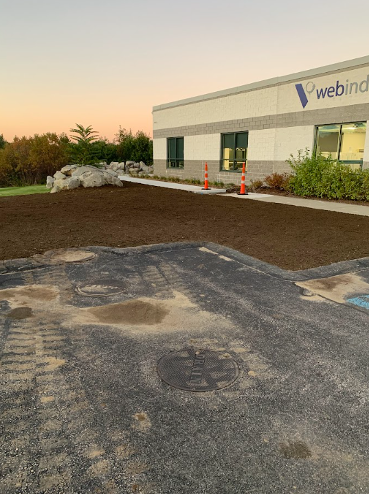 Industrial building exterior at sunset with fresh asphalt, dirt piles, and orange safety cones