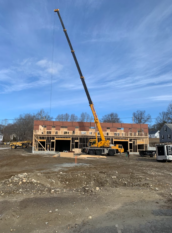 Construction site with a tall yellow crane lifting materials near a partially built brick building under a blue sky