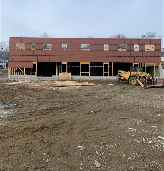 Partially built brick commercial building with open framing and a yellow loader on a muddy construction site