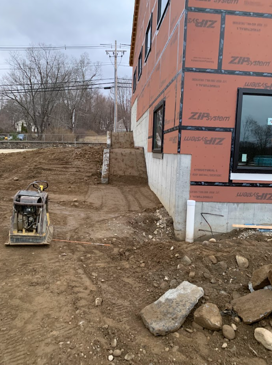 Construction site beside red-brick building with dirt path and a compactor on bare ground