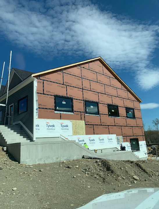Partially built brick house with roof and windows on a dirt lot under a blue sky