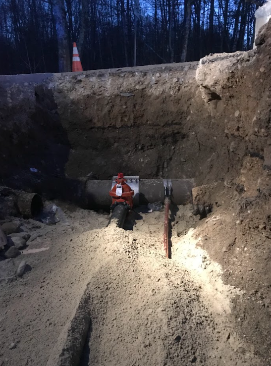 Excavation site at dusk with a worker in orange gear standing near a trench wall and exposed dirt slope.