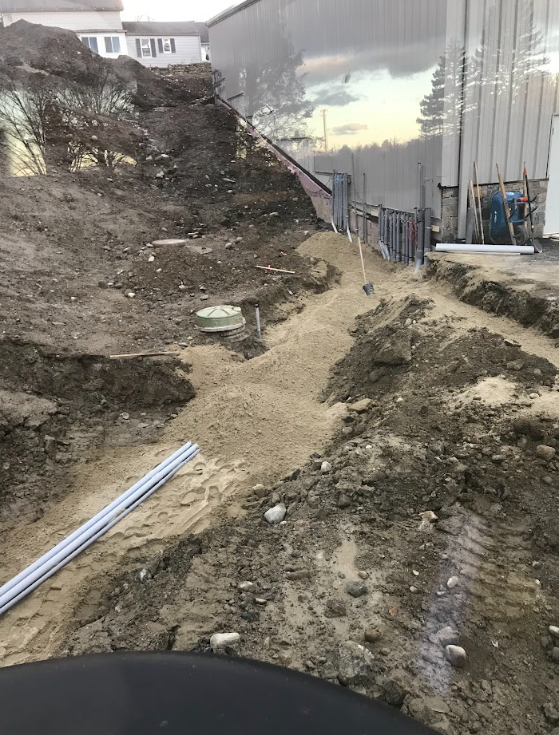 Uneven muddy construction path beside a building, with dirt piles, pipes, and fencing.