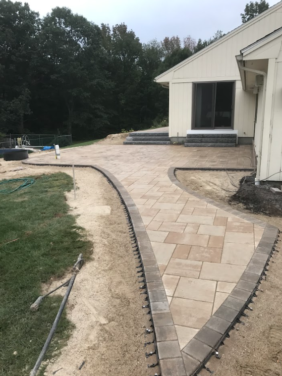Curved tan paver walkway beside a white house, leading through a landscaped yard