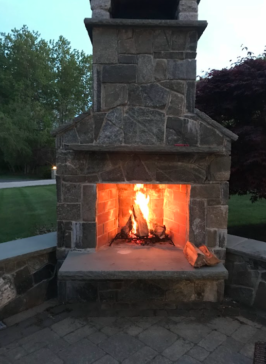 Stone outdoor fireplace with a burning fire at dusk