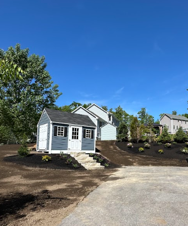 Small gray cottage with white trim on a landscaped slope under a clear blue sky
