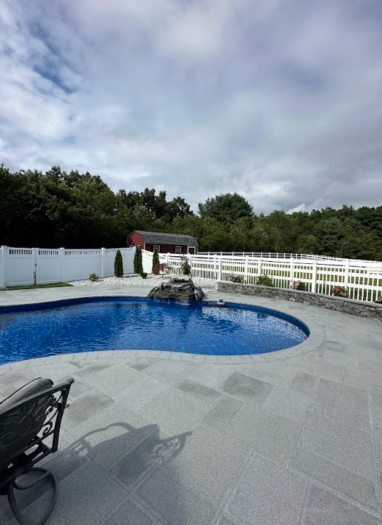 Backyard pool with white fence, blue water, and a small fountain under a cloudy sky