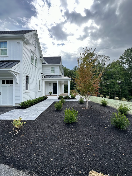 White two-story house with a dark gravel front yard, stone walkway, and shrubs under a cloudy sky
