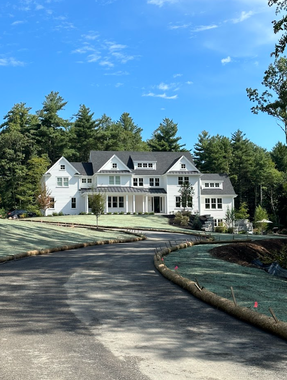 Large white mansion with a curved driveway, surrounded by trees under a clear blue sky
