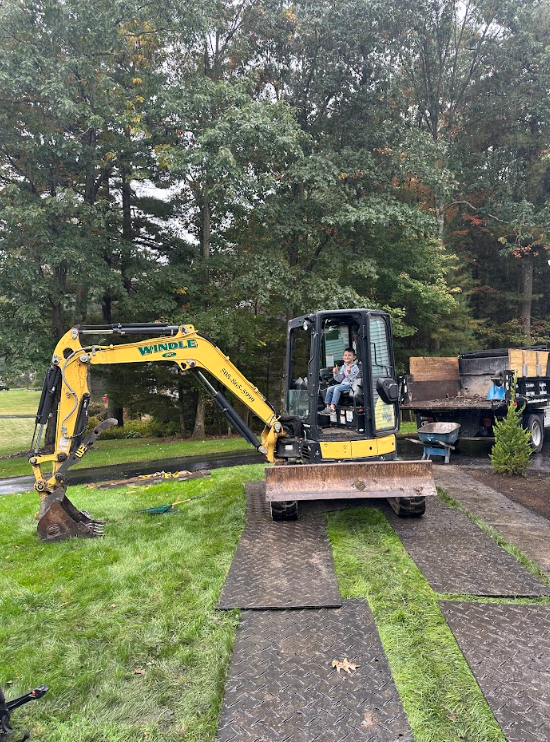 Yellow excavator on a grassy driveway with trees in the background