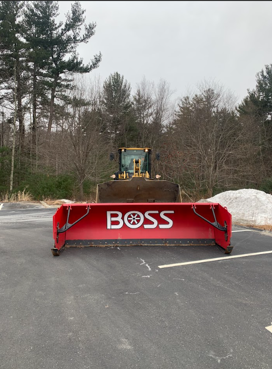 Red BOSS snowplow parked on a paved lot with trees in the background