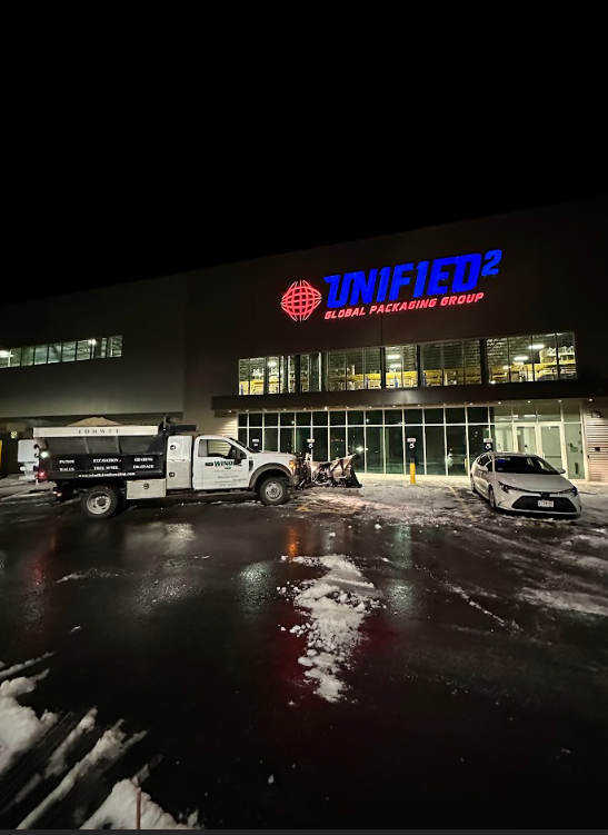 Snowy night outside a lit truck dealership with parked white vehicles and wet pavement reflections