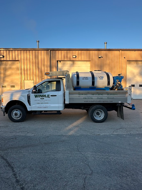 White utility truck with a large tank parked in front of a wooden building at sunset
