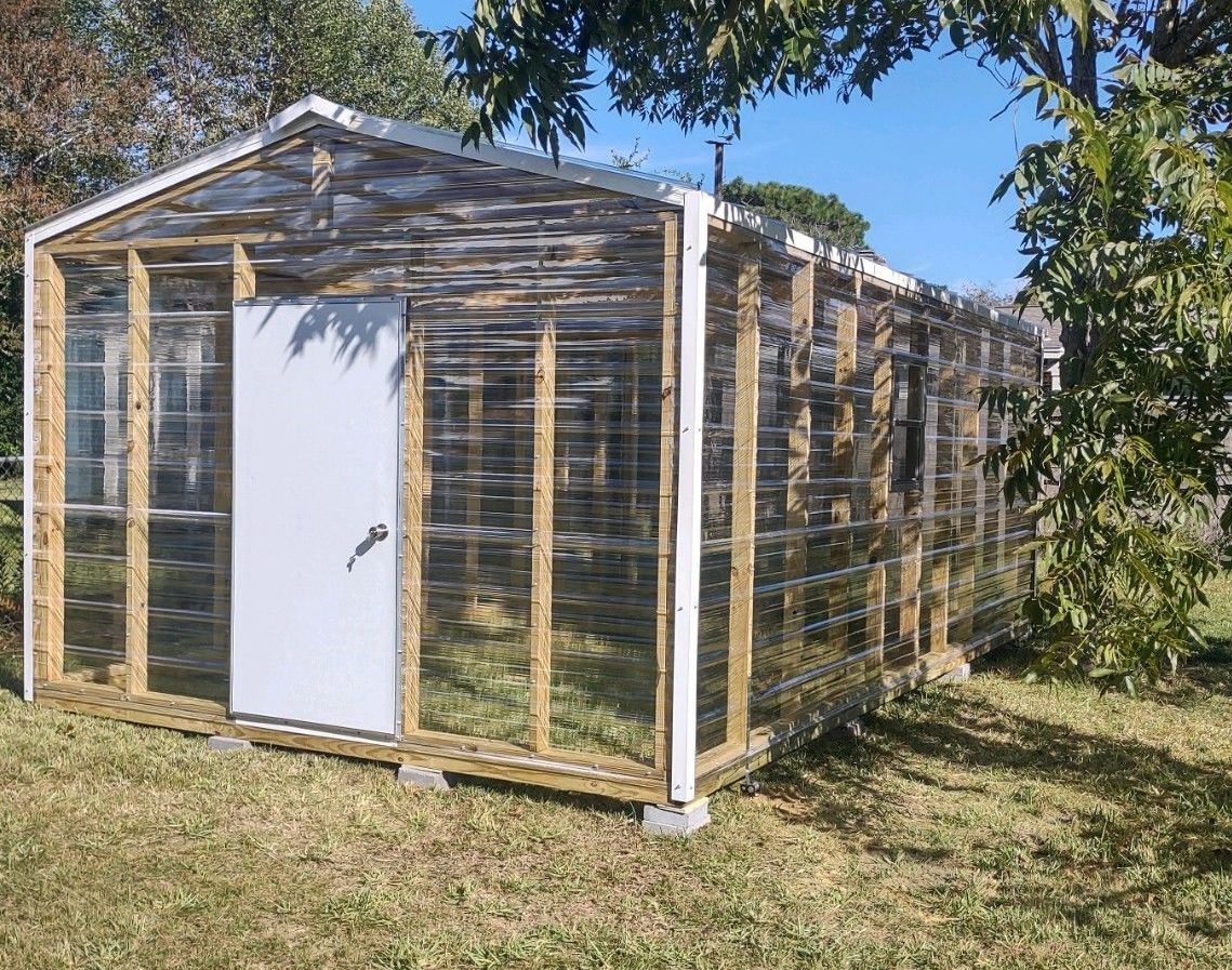 A greenhouse is sitting in the middle of a grassy field.
