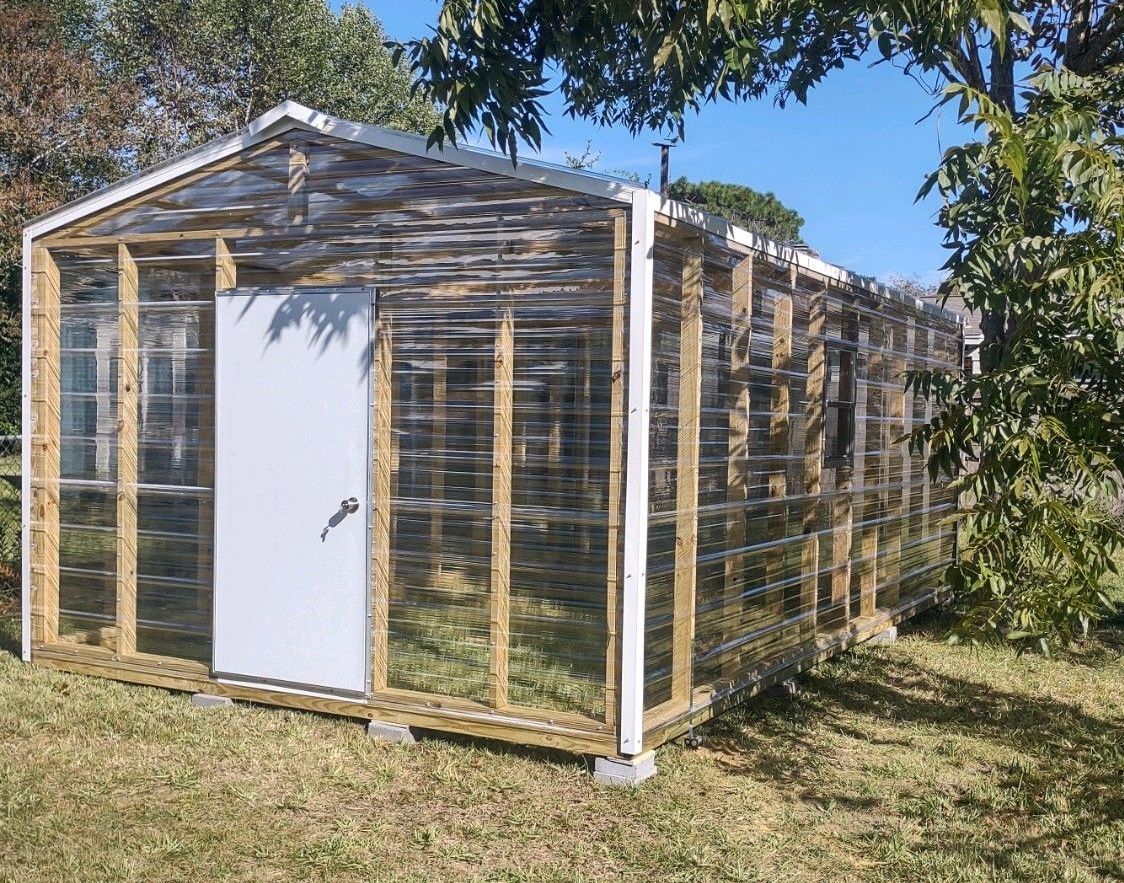 A greenhouse with a white door is sitting in the grass.