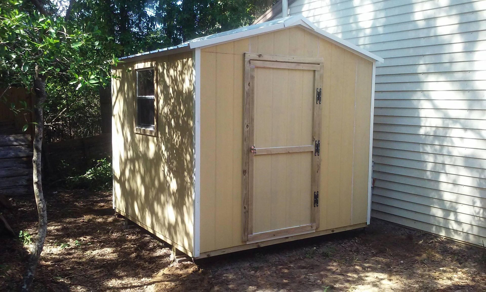 A small wooden shed is sitting in the backyard next to a house.