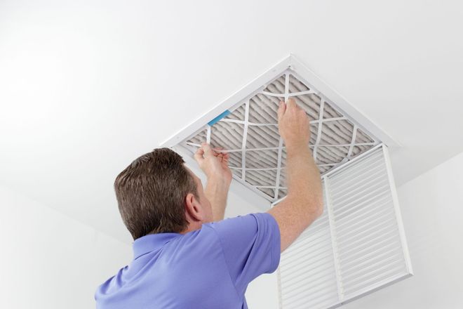 Man replacing air filter in ceiling vent.