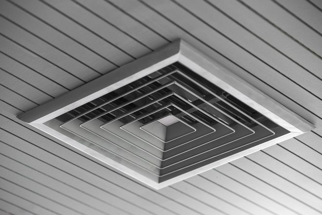 Square air vent on a white, slatted ceiling.