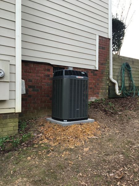 Dark green air conditioning unit on a concrete pad next to a brick wall.