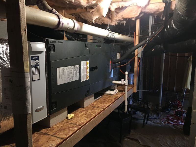 HVAC system components, including a furnace and air handler, mounted on a wooden shelf in a basement.