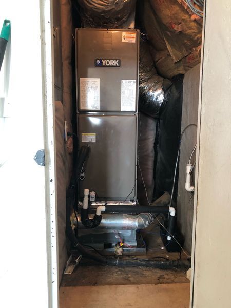 York HVAC unit installed in a utility closet with ductwork and pipes.
