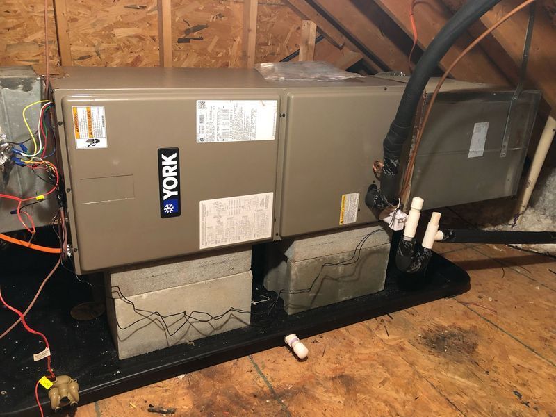 York HVAC unit in an attic, sitting on concrete blocks, with electrical wiring visible.