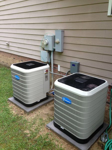 Two outdoor HVAC units sit on concrete pads, near a building with electrical boxes.
