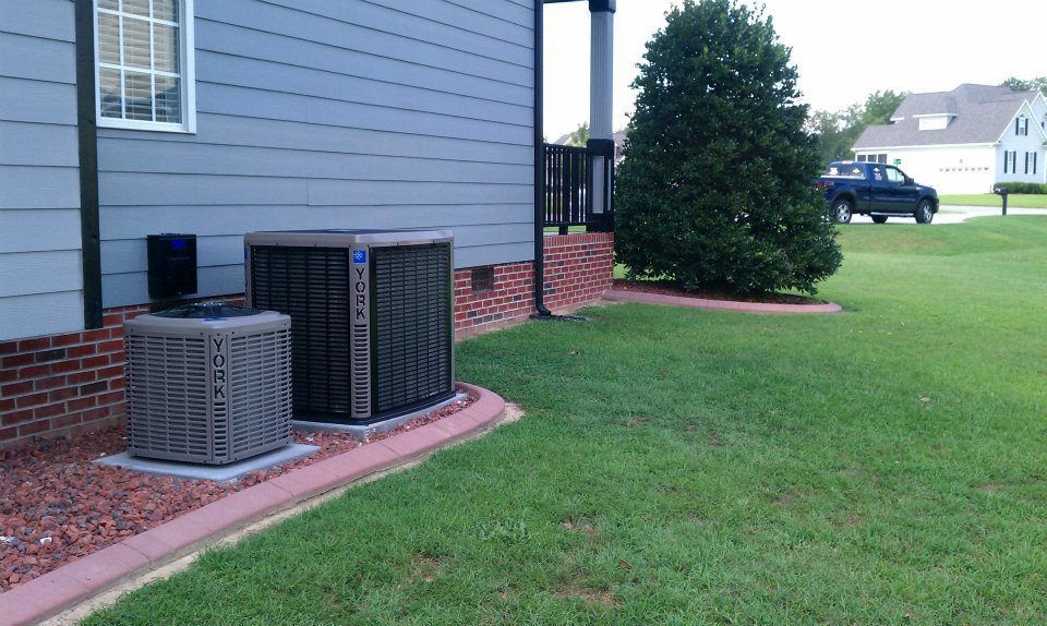 AC units next to a gray house, on red gravel border, with green lawn.