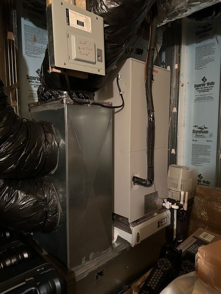 A HVAC system with ductwork in a basement. The unit is gray and white, with black ducting and wires.