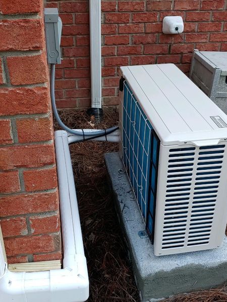 AC unit next to a brick wall with electrical box and downspout.