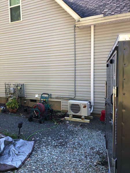 Exterior view of a house with air conditioning units, metal conduit, and gravel ground.