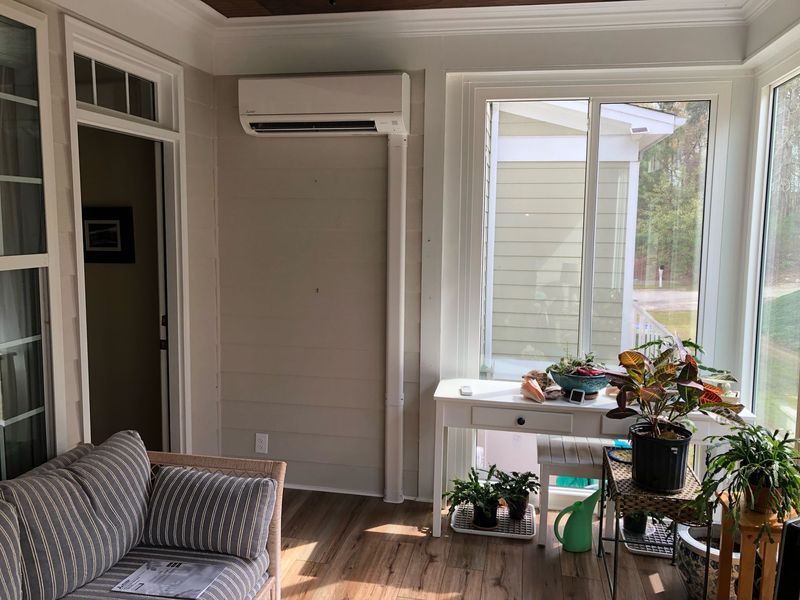Sunroom with air conditioner unit above a door, plants, a white table, and a striped sofa.