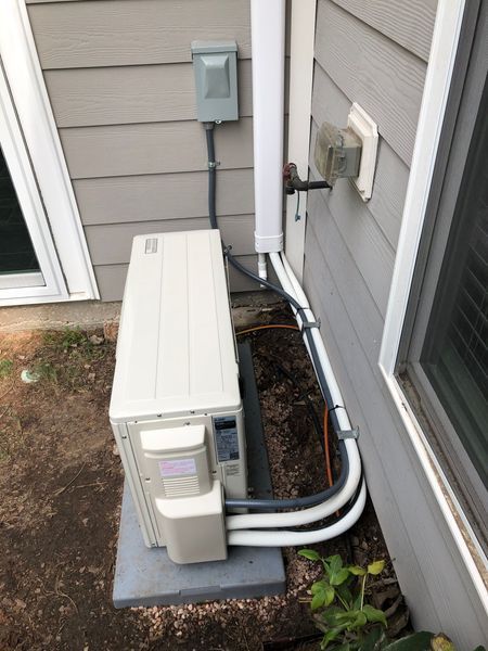 Outside HVAC unit near a building with electrical conduit and gas line. Gray siding and concrete base.