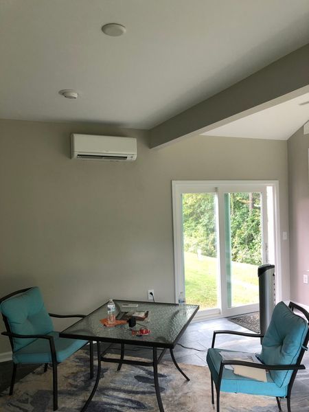 A room with a glass table, teal chairs, and a white air conditioning unit on the wall, near a sliding door.