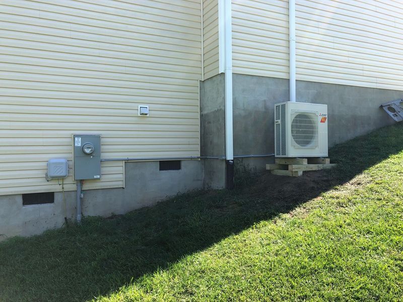 Exterior of a house with an air conditioning unit and electrical box, sitting on a grassy hill.