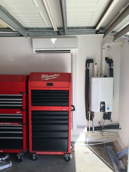 Red tool chests next to a white wall with an AC unit and a white water heater, mounted in a garage.