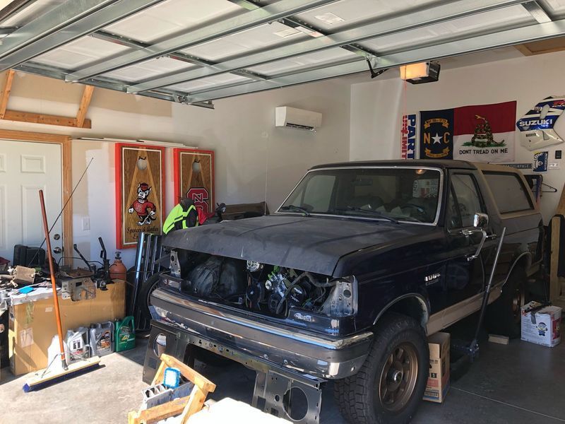 A partially disassembled dark blue Bronco truck in a garage with tools and wall art.