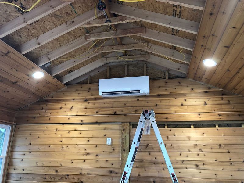 Interior of a wooden shed with installed air conditioner, recessed lights, and a ladder.