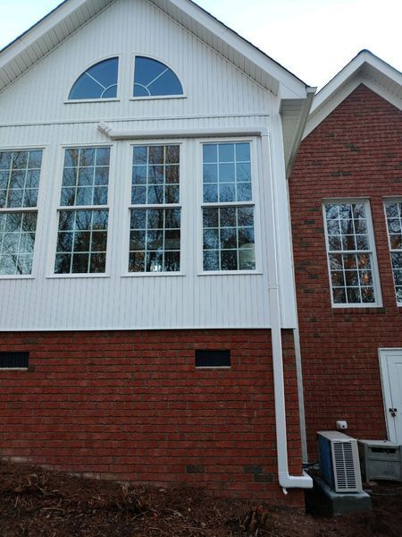 Exterior view of a white-sided building with large windows and a red brick foundation; a side structure is also visible.