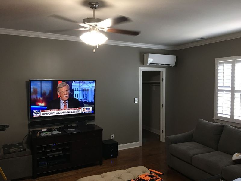 A living room with a TV showing news, couch, air conditioner, ceiling fan, and open closet door.
