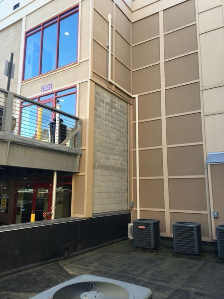Building exterior with tan panels, a concrete block wall, and air conditioning units on a flat roof.