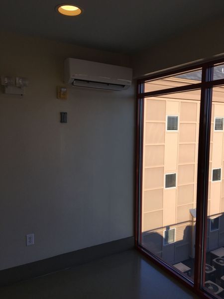 Interior room with a wall-mounted AC unit above a baseboard. A large window looks out onto a building.