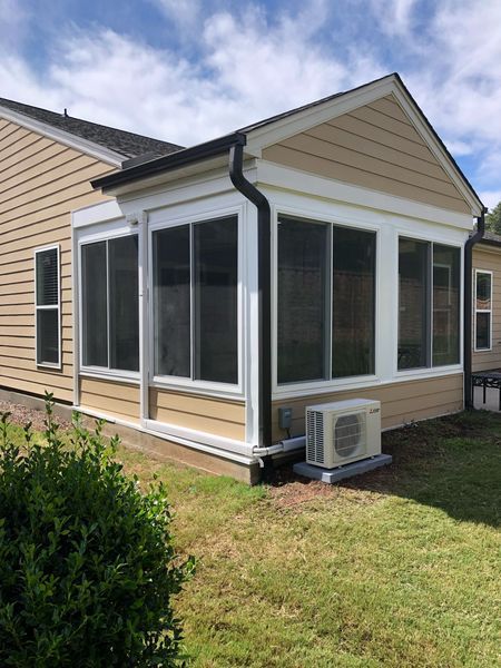 Sunroom addition with tan siding, large windows, and an air conditioning unit.