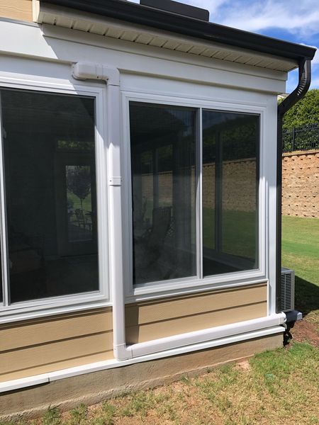 Sunroom with white-framed windows and tan siding. Green grass and brick wall are in the background.